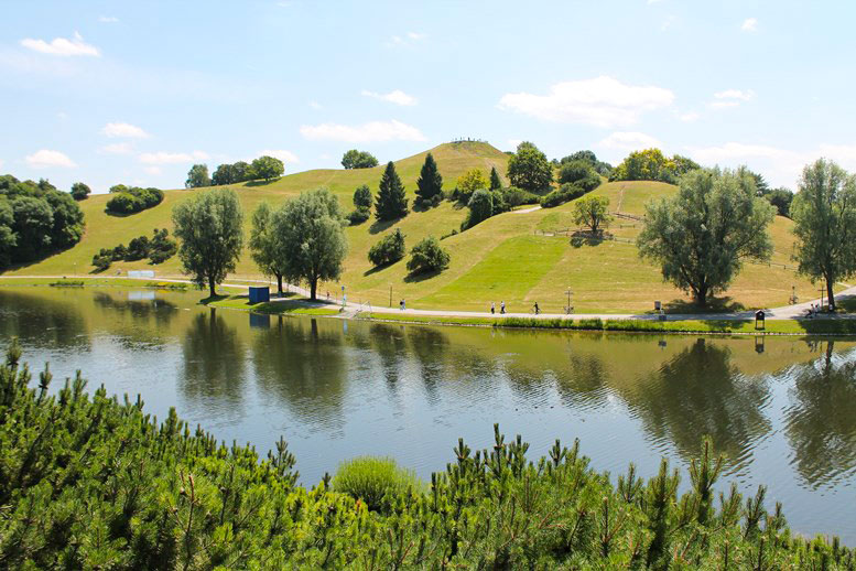 Grüne Idylle im Olympiapark: Der Olympiasee mit dem Olympiaberg im Hintergrund.